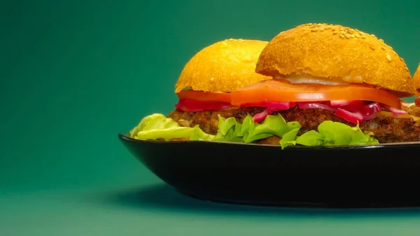 Homemade hamburgers on black plate on uniform green background — Stock Photo, Image