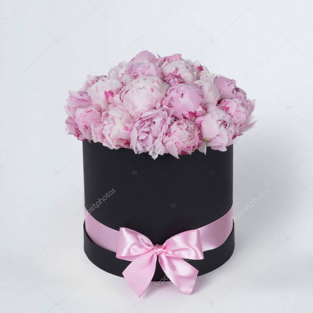 Luxury beautiful pink bouquet of peony flowers round black box with bow on gray background
