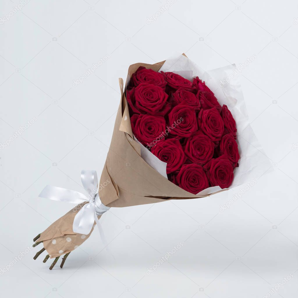 A bouquet of beautiful flowers of red roses in a kraft packing on a gray background