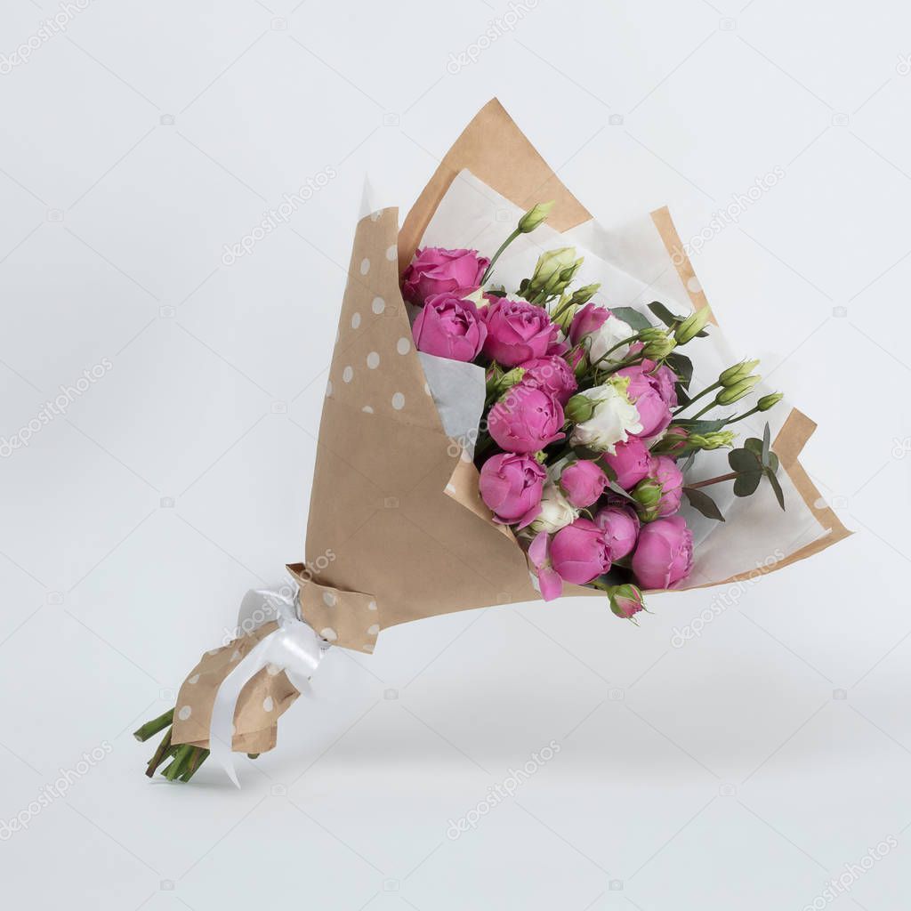 Bouquet of beautiful pink peony flowers in kraft packaging on a gray background