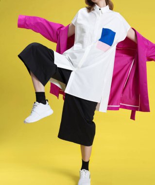 Siyah pantolon ve beyaz gömlek ve pembe kısa yağmurluk sarı bir arka plan üzerinde poz uzun saçlı güzel sarışın kız