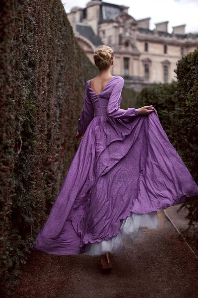 Beautiful young woman runs in a luxurious long lilac dress in Paris in a park near the Louvre