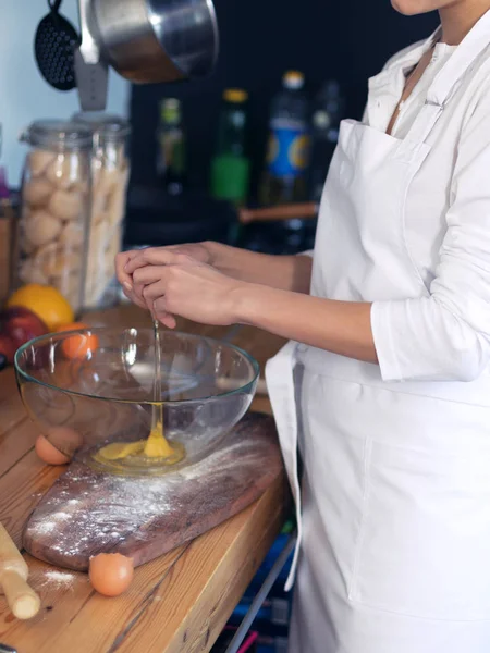 Girl cook in a white apron in the equipped kitchen, cooks eggs and flour