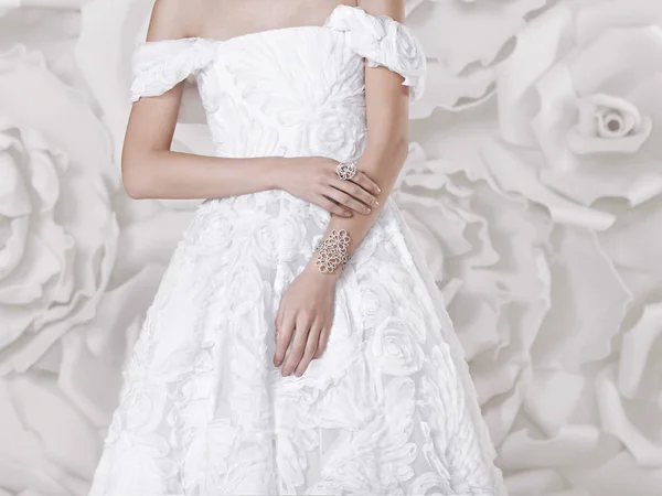 白い花の壁の背景に宝石類で レースの白い高級ウェディング ドレスの美しい少女が立っています — ストック写真
