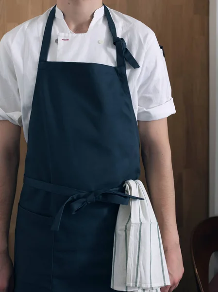 Male cook in blue apron against the background of a wooden wall
