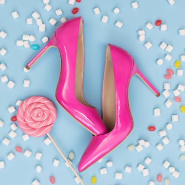 Tasarım, reklam ya da arka plan için güzel bir set, lüks kadınların pembe deri topuklu ayakkabıları mavi arka planda şeker ve şekerlemelerle sunuluyor.