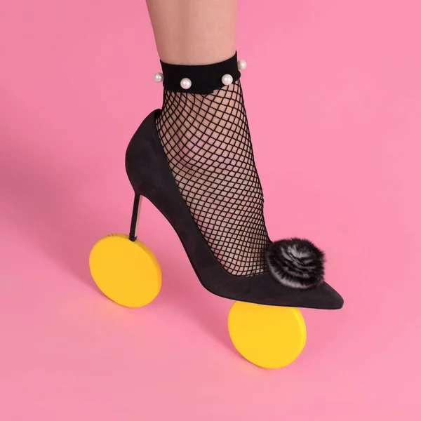 Luxurious beautiful female leg in black mesh tights and a black high-heeled shoe with two yellow wheels, pink background, shoe advertising, banner, mock-up