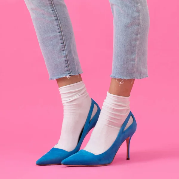 Luxurious elegant suede blue vibrant high-heeled shoes on female legs in fashionable trainers and socks, on a pink background, shoe advertising, banner, mock-up