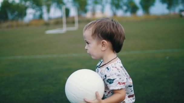 El niño sostiene la pelota en sus manos en el campo de fútbol. — Vídeo de stock