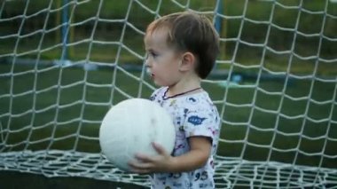 Küçük çocuk topu futbol sahasına onun elinde tutuyor