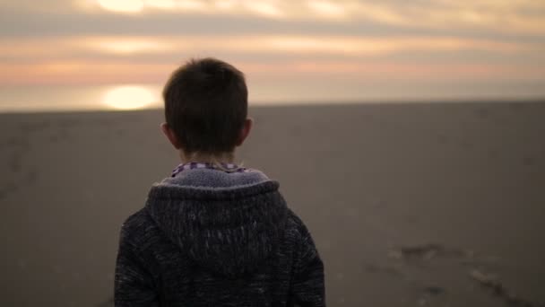 El niño camina por la playa al atardecer . — Vídeos de Stock