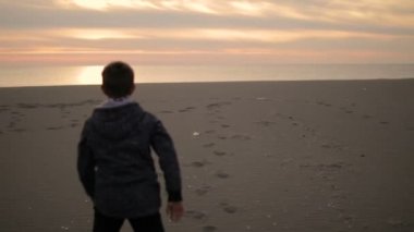 Çocuk plaj boyunca gün batımında yürür..