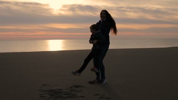 Ein glückliches Kind. eine Mutter spielt mit dem Kind. Die Mutter umkreist das Kind, indem sie seine Hände nimmt. Gegenlicht. schöner Sonnenuntergang. — Stockvideo