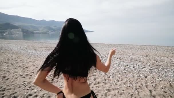 性感的女孩在黑色比基尼泳装与一个美丽的运动人物跳舞在海边 — 图库视频影像