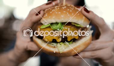 Bir genç kız büyük bir iştah açıcı çizburger vardır. Yakın çekim elinde tutar. Bir kadın onu ısırır ve büyük zevk alır. Yakın çekim. Slowmotion 60fps