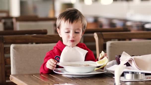 Маленький хлопчик їсть суп і хліб за столом — стокове відео
