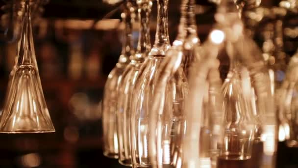 Copos de vinho limpos pendurados de cabeça para baixo acima de um rack de bar no restaurante. — Vídeo de Stock
