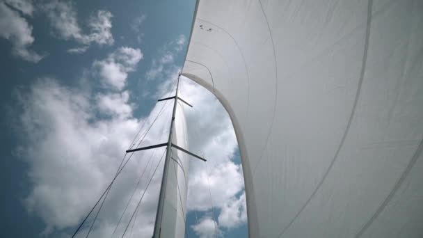 The wind blows into the sails of the yacht which goes through the water against the backdrop of a beautiful blue sky with clouds close-up — Stock Video