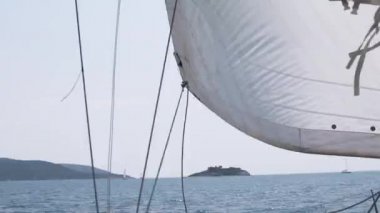 Rüzgar, güzel mavi bir gökyüzünün arka planında suyun içinden geçen yatın yelkenlerine esiyor.