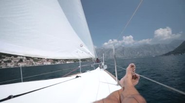 Yelkenli yattaki bir adam güvertede uzanır ve zevk alır Rüzgar yelkene eser.