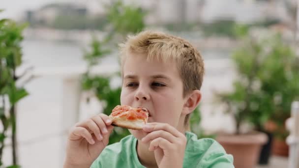 Een jongen van 10 jaar eet met plezier pizza — Stockvideo