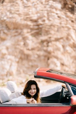Mutlu kadın güzel manzaralı kırmızı üstü açık bir arabada oturuyor.