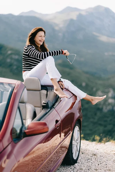 Mujer feliz se sienta en un coche convertible rojo con una hermosa vista — Foto de Stock