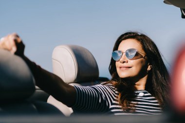 Mutlu kadın güzel manzaralı kırmızı üstü açık bir arabada oturuyor.