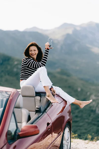 Happy woman sits in a red convertible car with a beautiful view — Stock Photo, Image