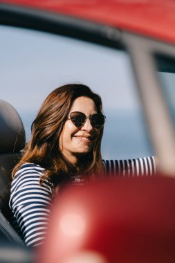 Mutlu kadın güzel manzaralı kırmızı üstü açık bir arabada oturuyor.