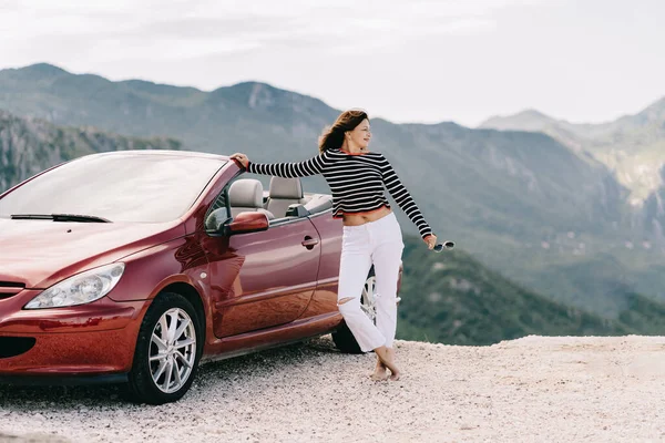 Mujer feliz estancia cerca de coche convertible rojo con una hermosa vista Imagen De Stock