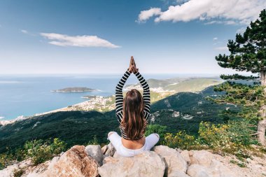Nilüfer çiçekli kız, güzel deniz manzaralı bir dağın tepesinde poz veriyor.