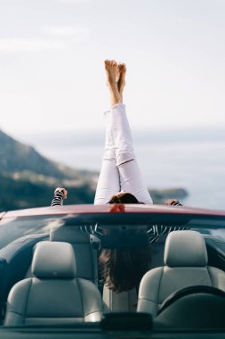 Mutlu kadın güzel manzaralı kırmızı üstü açık bir arabada oturuyor.