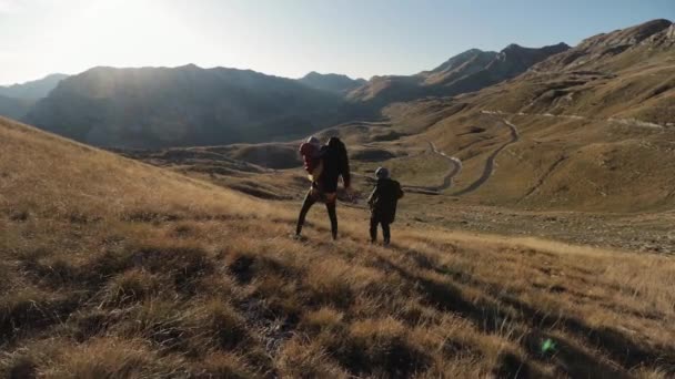 Genç bir aile, batan güneşin ışınlarında bir dağ yamacında duruyor. — Stok video