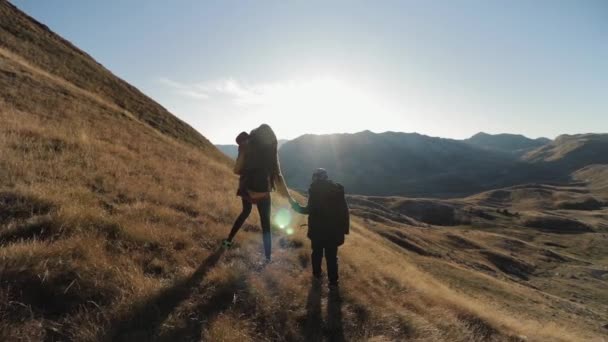 Una familia joven se encuentra en una ladera de la montaña bajo los rayos del sol poniente — Vídeo de stock