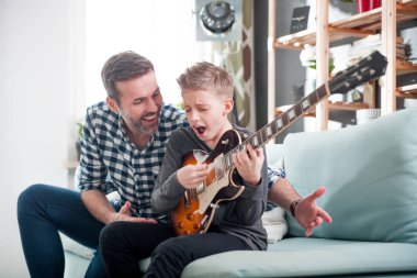 Oğul ve baba evde kanepede elektro gitar çalmak