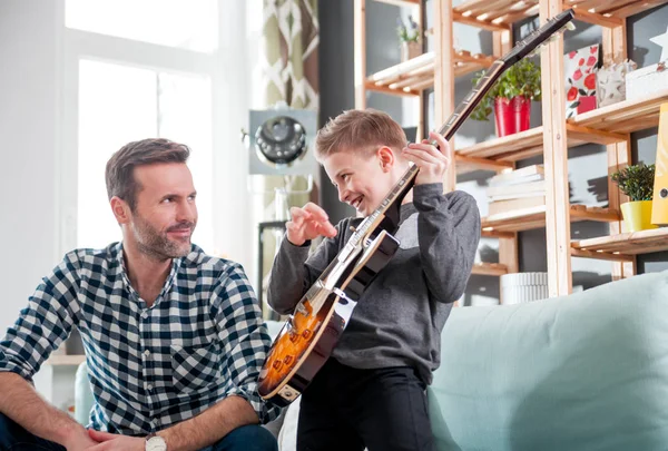 Son and father playing electric guitar on sofa at home