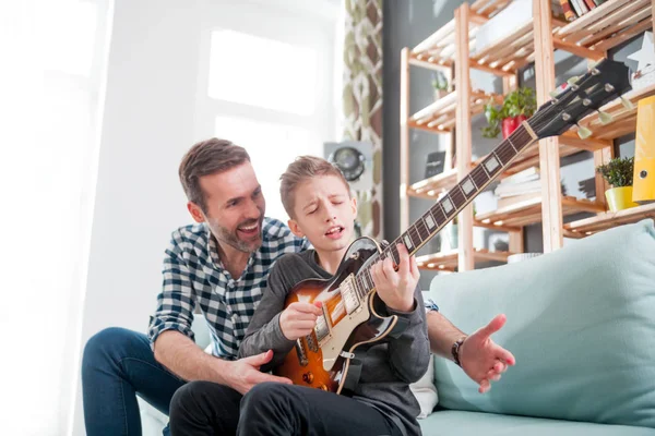 Son and father playing electric guitar on sofa at home