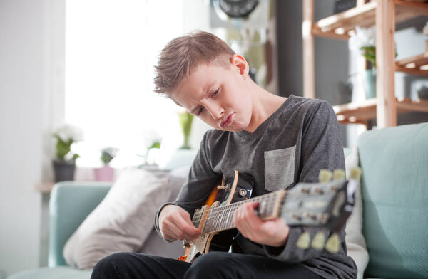 Young boy playing electric guitar on sofa at home