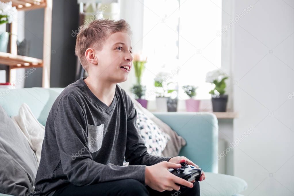 Excited young boy playing game on console at home