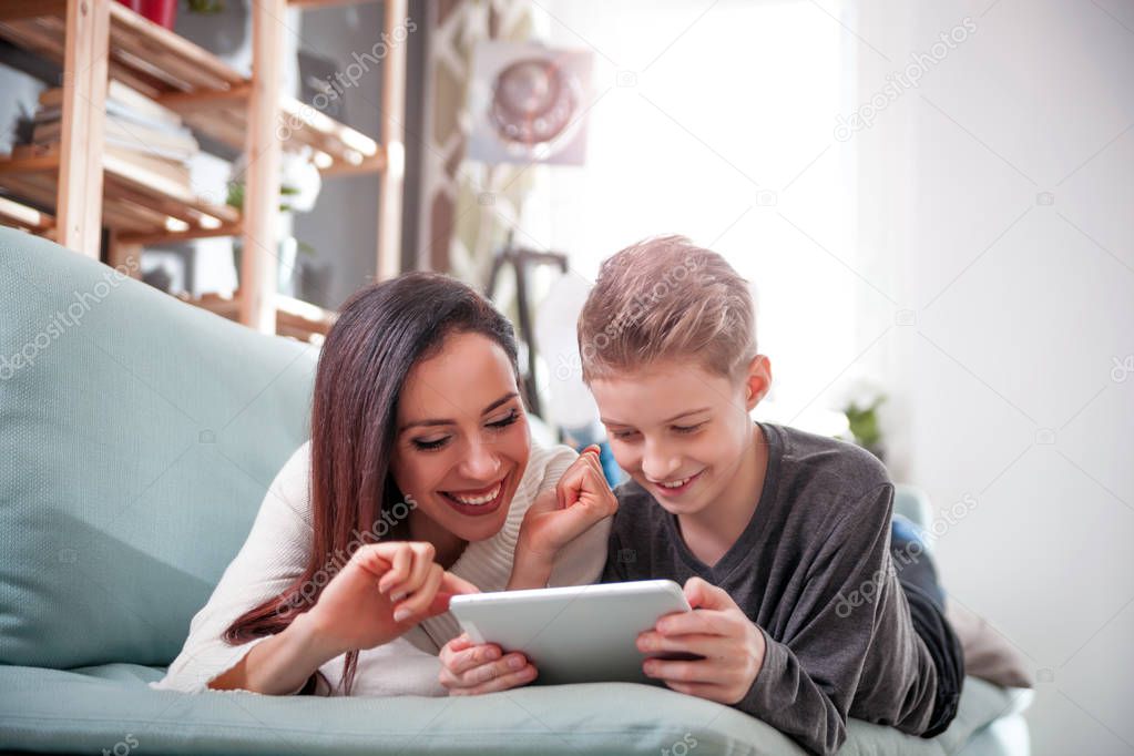 Mother and son lying on sofa and using digital tablet at home