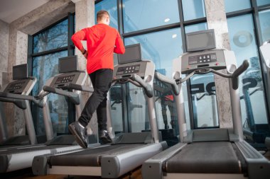 Spor salonunda koşu bandında koşan genç adam.