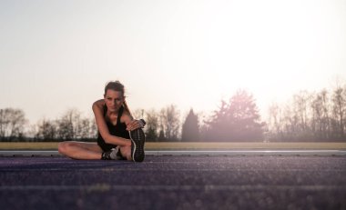 genç atletik kadın Stadyumu koşu parkuru üzerinde günbatımında germe