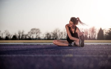 genç atletik kadın Stadyumu koşu parkuru üzerinde günbatımında germe
