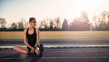 genç atletik kadın Stadyumu koşu parkuru üzerinde günbatımında germe