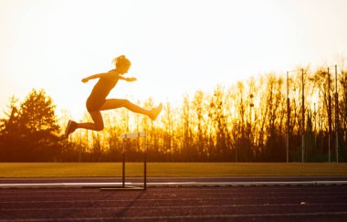 Stadyum yolda çalışan ve gün batımında engel atlama atletik kadın