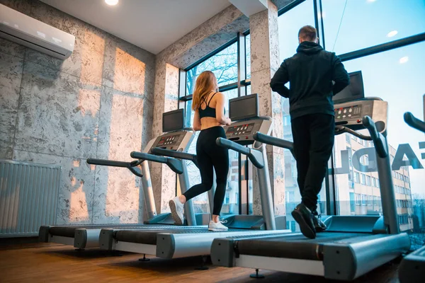 Young couple running on treadmill machine at fitness gym