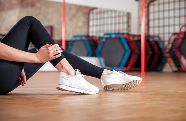 Injured fit woman feeling pain in ankle at fitness gym