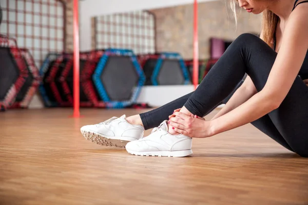 Injured fit woman feeling pain in ankle at fitness gym