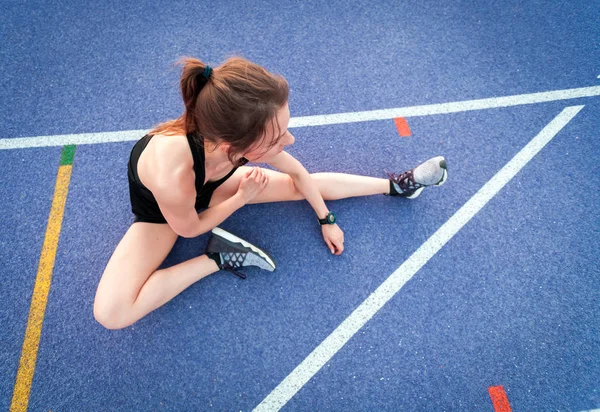 Young athletic woman resting  on studium track after training